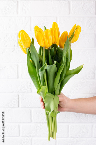 A man's hand holds a beautiful bouquet of yellow tulips against a white brick wall. The concept of the celebration. Greeting card for women's Day on March 8, Happy Easter, Valentine's day