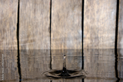 Splash and ripples on water from fallen raindrop on wooden background.