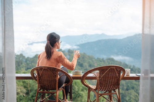 Happy woman drinking coffee and eating breakfast against mountain view at countryside home or homestay in the morning. Vacation, blogger, SoloTravel, journey, trip and relaxing concept photo