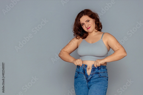 weight loss and overweight problem. a fat woman in a tank top and jeans is trying to button up or put on a size down jeans. disappointment from a non-athletic figure