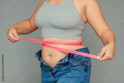 weight loss and overweight problem. a fat woman in a tank top and jeans is disappointed and upset by the extra centimeters on the ruler. photo on gray photo photo