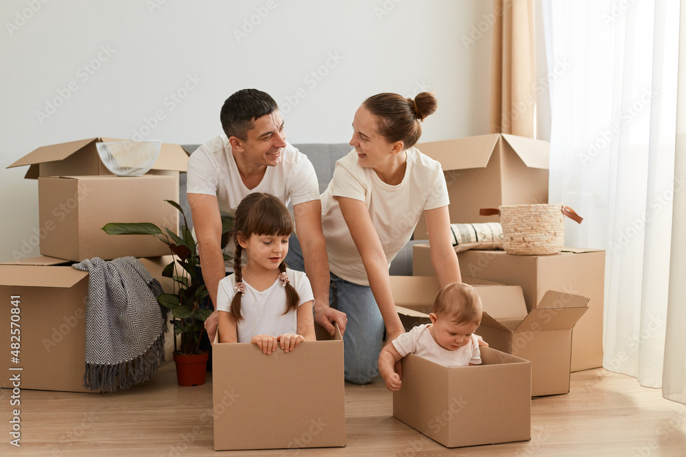 Happy couple with their children in a cardboard boxes having fun together in a relocating day, playing with kids and expressing love and happiness, finally buying their own house. Happy couple with their children in a cardboard boxes having fun together in a relocating day, playing with kids and expressing love and happiness, finally buying their own house.