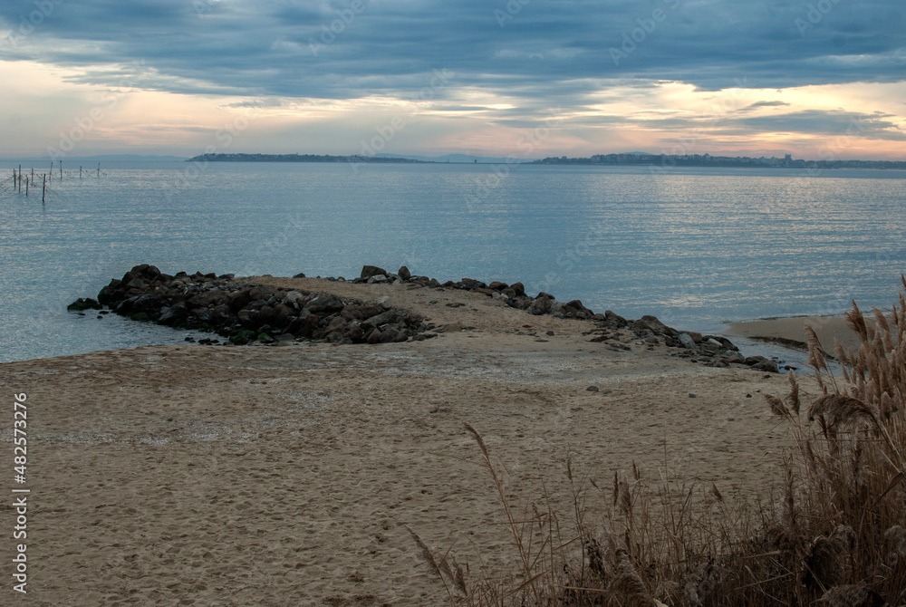 Lanscape with sand beach, quay and calm sea waters at cloudy sunset