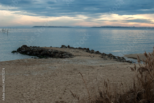 Lanscape with sand beach  quay and calm sea waters at cloudy sunset