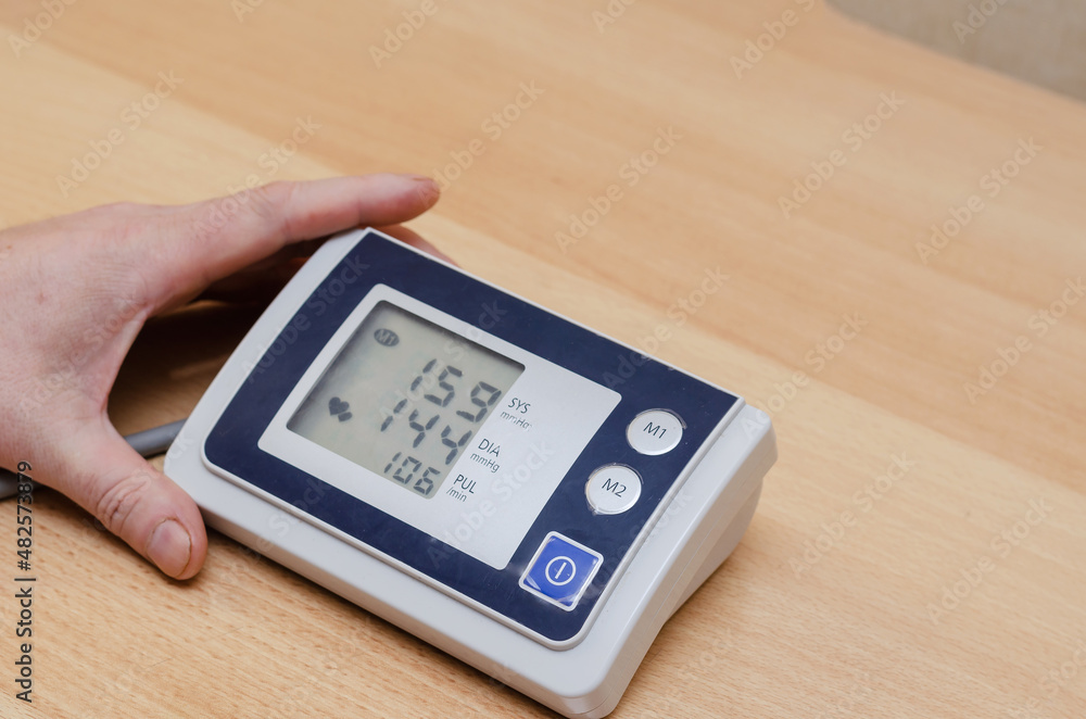 A man's hand holds a digital blood pressure monitor on the table A man's hand holds a digital blood pressure monitor on the table