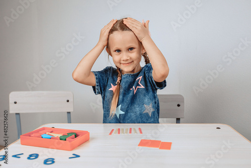 Portrait of a cute, affectionate and kind girl sitting at a table surrounded by puzzles and putting her hands on her head. Shocked girl. photo with noise