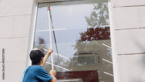 An employee of a professional cleaning service in overalls washes the glass of the windows of the facade of the building. Showcase cleaning for shops and businesses