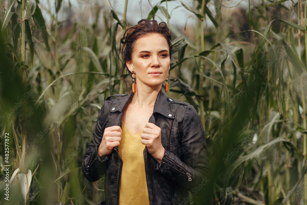 Portrait of an adorable cute and attractive model holding her black jacket and posing against a backdrop of grass and leaves. Attractiveness concept