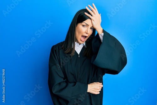 Young hispanic woman wearing judge uniform surprised with hand on head for mistake, remember error. forgot, bad memory concept. photo