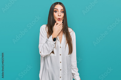 Young beautiful woman wearing casual white shirt looking fascinated with disbelief, surprise and amazed expression with hands on chin