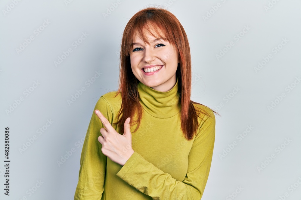 Fototapeta premium Redhead young woman wearing turtleneck sweater smiling cheerful pointing with hand and finger up to the side