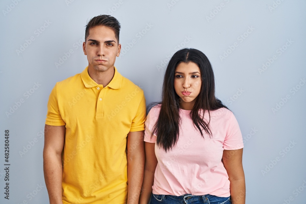 Young couple standing over isolated background puffing cheeks with funny face. mouth inflated with air, crazy expression. Young couple standing over isolated background puffing cheeks with funny face. mouth inflated with air, crazy expression.