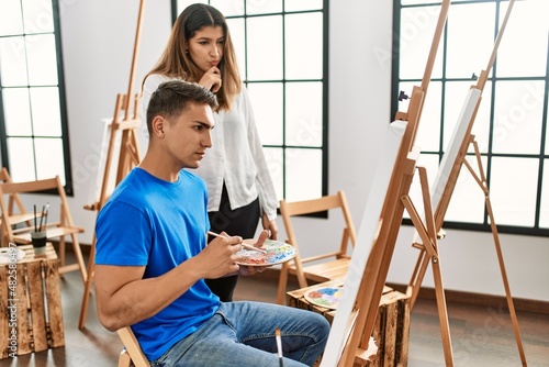 Student and teacher with serious expression painting at art school.