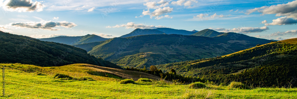 panoramic mountain landscape with green meadows in evening light. beautiful summer scenery with clouds on a blue sky