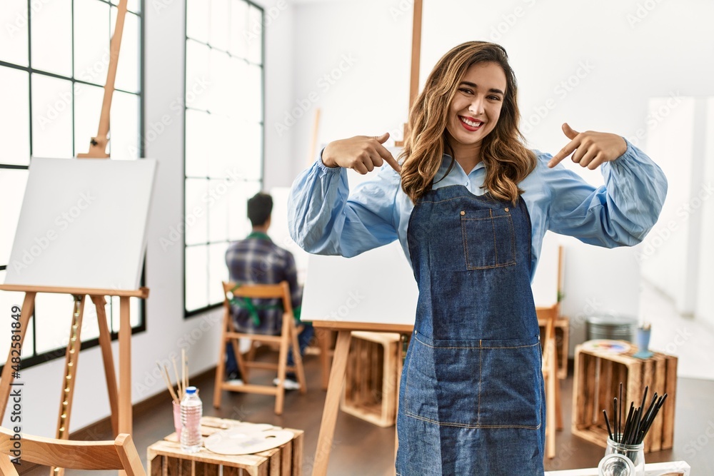 Young artist woman at art studio looking confident with smile on face, pointing oneself with fingers proud and happy. Young artist woman at art studio looking confident with smile on face, pointing oneself with fingers proud and happy.