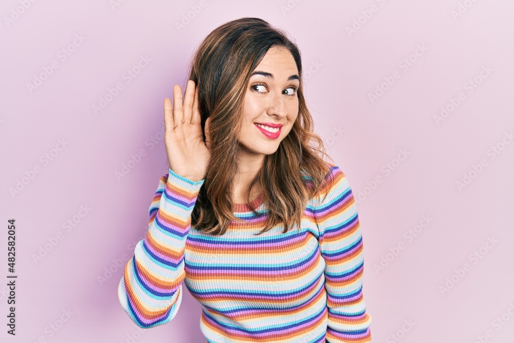 Young hispanic girl wearing casual clothes smiling with hand over ear listening an hearing to rumor or gossip. deafness concept. Young hispanic girl wearing casual clothes smiling with hand over ear listening an hearing to rumor or gossip. deafness concept.