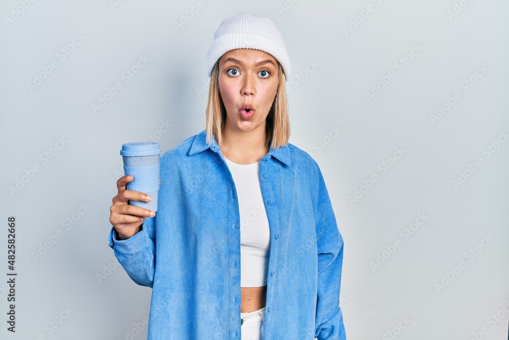 Beautiful blonde woman drinking a take away cup of coffee scared and amazed with open mouth for surprise, disbelief face Beautiful blonde woman drinking a take away cup of coffee scared and amazed with open mouth for surprise, disbelief face