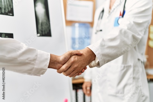 Two doctor celebrating achievement with handshake at the clinic office.