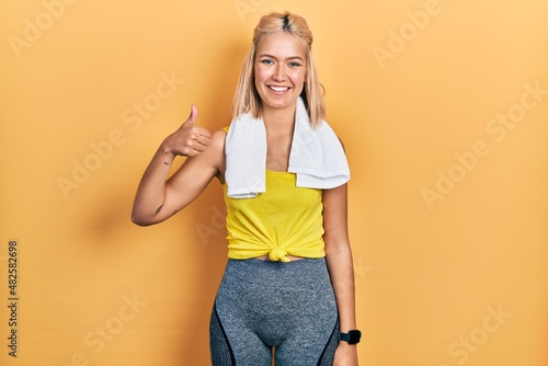Beautiful blonde sports woman wearing workout outfit doing happy thumbs up gesture with hand. approving expression looking at the camera showing success.