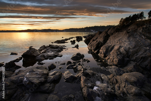 Winter is set in fjord. The sun is painting colors on the sky and the water is calm. Beautiful place just outside Oslo, Norway called Snarøya. 