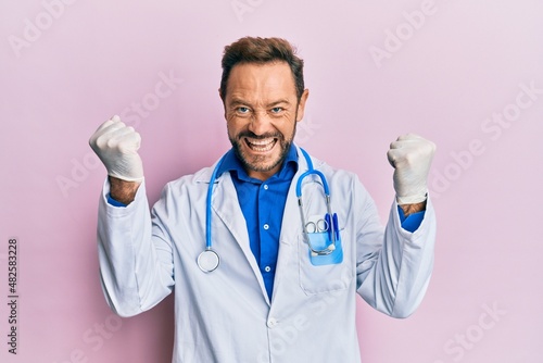 Middle age man wearing doctor uniform and stethoscope screaming proud  celebrating victory and success very excited with raised arms