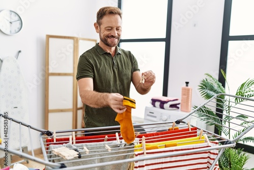 Middle age hispanic man hanging clothes at clothesline at laundry room