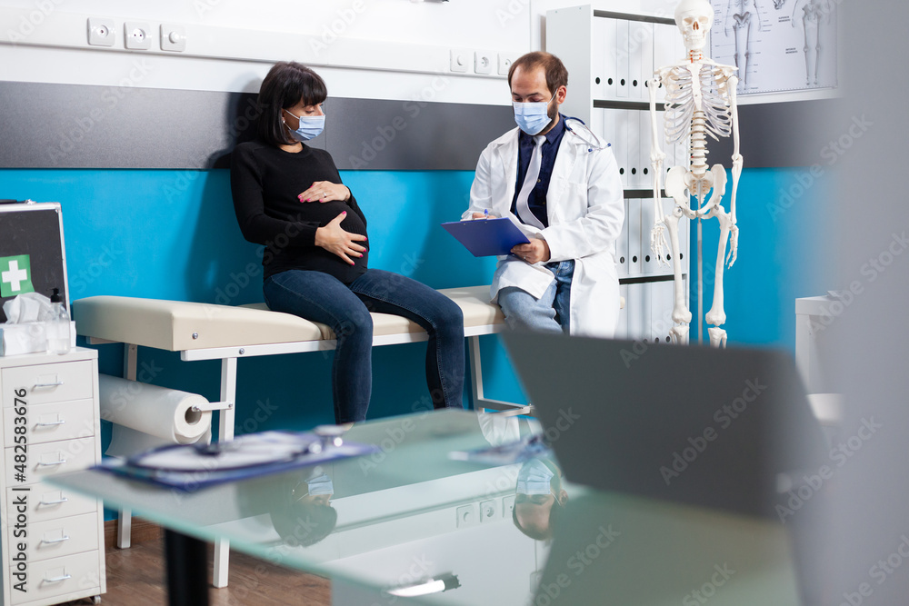 Fototapeta premium Obstetrician consulting expectant patient at checkup appointment. General practitioner and pregnant woman doing medical examination, discussing about childbirth support in cabinet.
