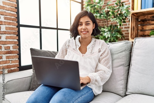 Young latin woman using laptop sitting on sofa at home