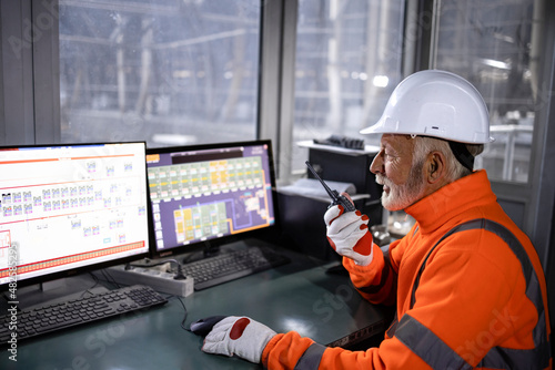 Industrial worker in safety equipment sitting in factory control room monitoring production process and talking on radio communication. photo