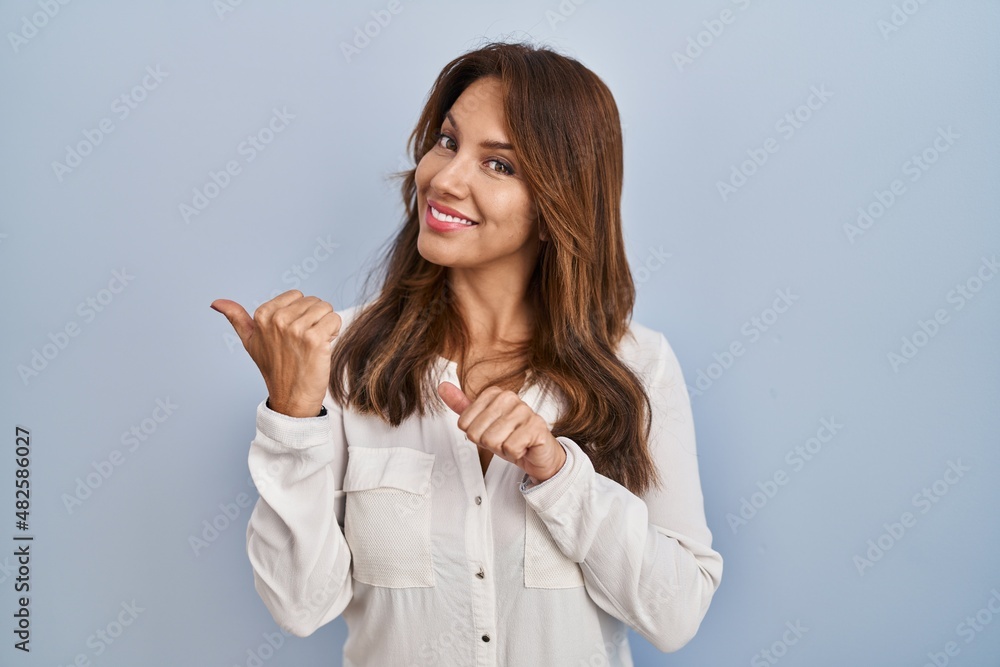 Hispanic woman standing over isolated background pointing to the back behind with hand and thumbs up, smiling confident Hispanic woman standing over isolated background pointing to the back behind with hand and thumbs up, smiling confident