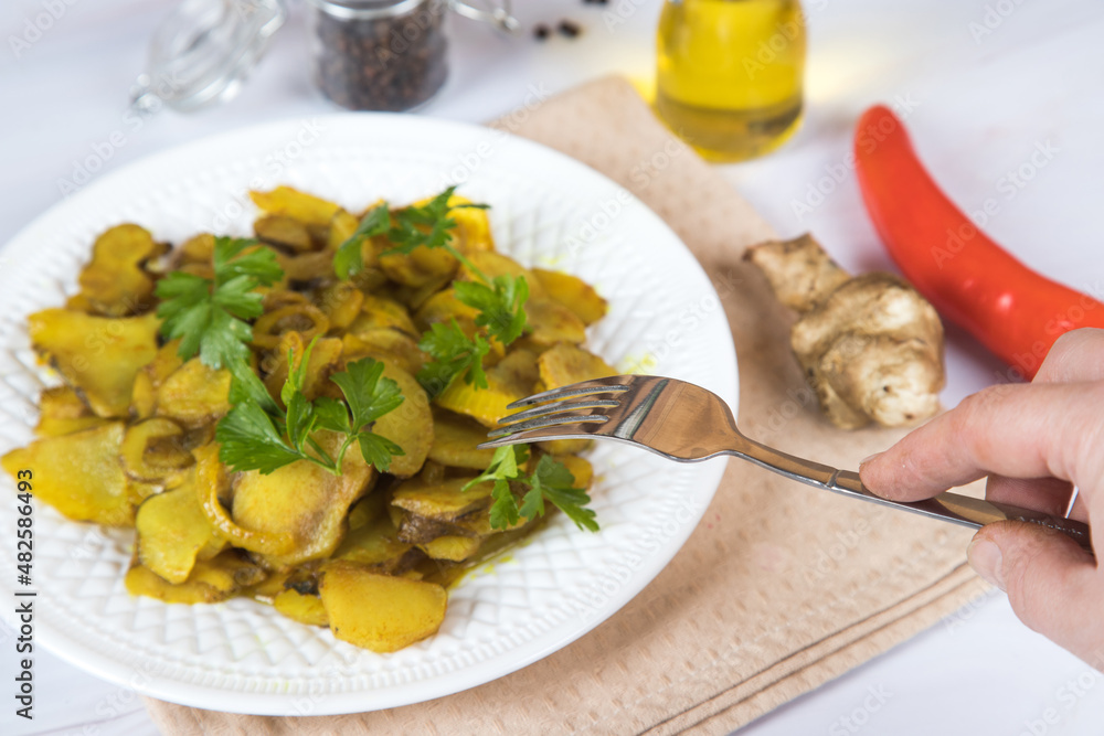 A woman's hand with a fork over a plate of fried jerusalem artichoke. A woman's hand with a fork over a plate of fried jerusalem artichoke.