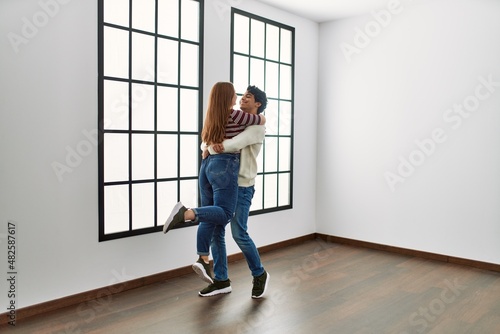 Young hispanic couple smiling happy and hugging standing at empty new home.