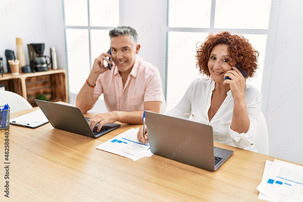 Obraz premium Middle age man and woman business workers using laptop and talking on the smartphone at office
