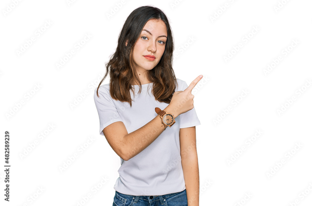 Young beautiful woman wearing casual white t shirt pointing with hand finger to the side showing advertisement, serious and calm face Young beautiful woman wearing casual white t shirt pointing with hand finger to the side showing advertisement, serious and calm face