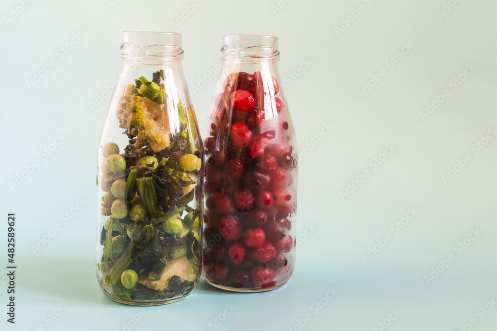 The concept of using fast-freezing products. Frozen green vegetables and red berries with ice crystals in transparent bottles on a light background. The concept of using fast-freezing products. Frozen green vegetables and red berries with ice crystals in transparent bottles on a light background.