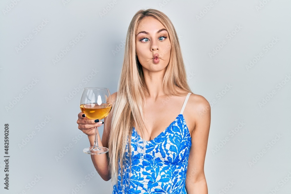 Young beautiful caucasian woman drinking a glass of white wine making fish face with lips, crazy and comical gesture. funny expression. Young beautiful caucasian woman drinking a glass of white wine making fish face with lips, crazy and comical gesture. funny expression.