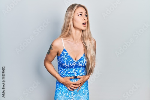 Young beautiful caucasian woman wearing summer dress with hand on stomach because nausea, painful disease feeling unwell. ache concept.