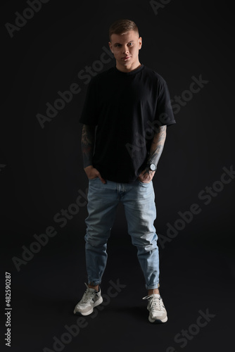 Young man with tattoos on black background