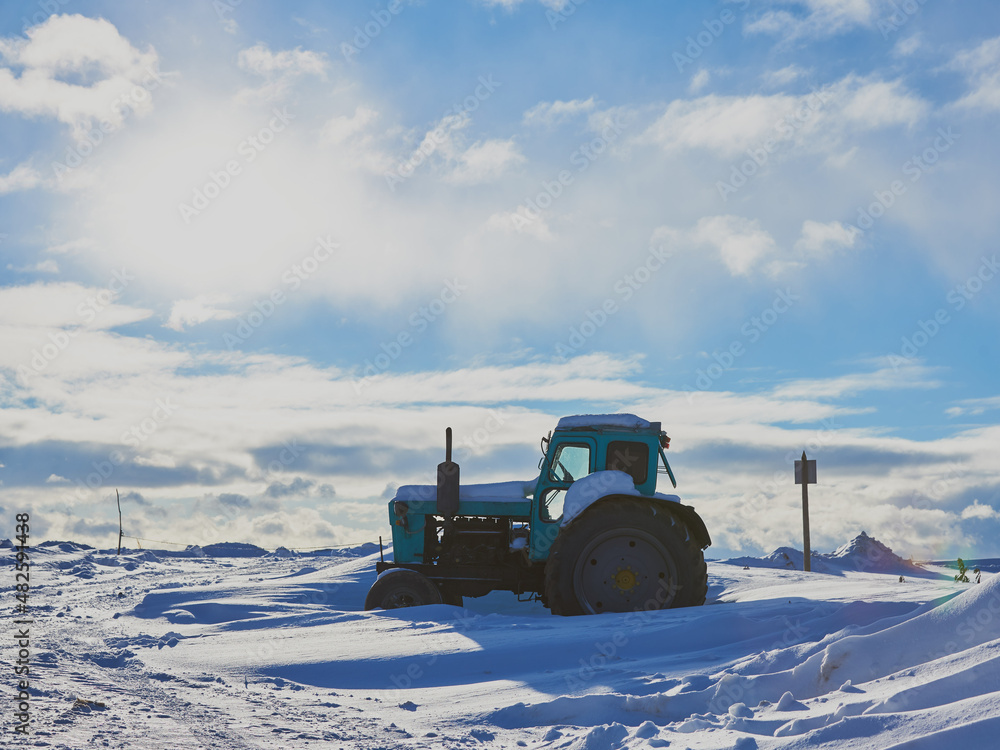 Tractor on a deserted snow-covered field against a cloudy sky. Tractor on a deserted snow-covered field against a cloudy sky.