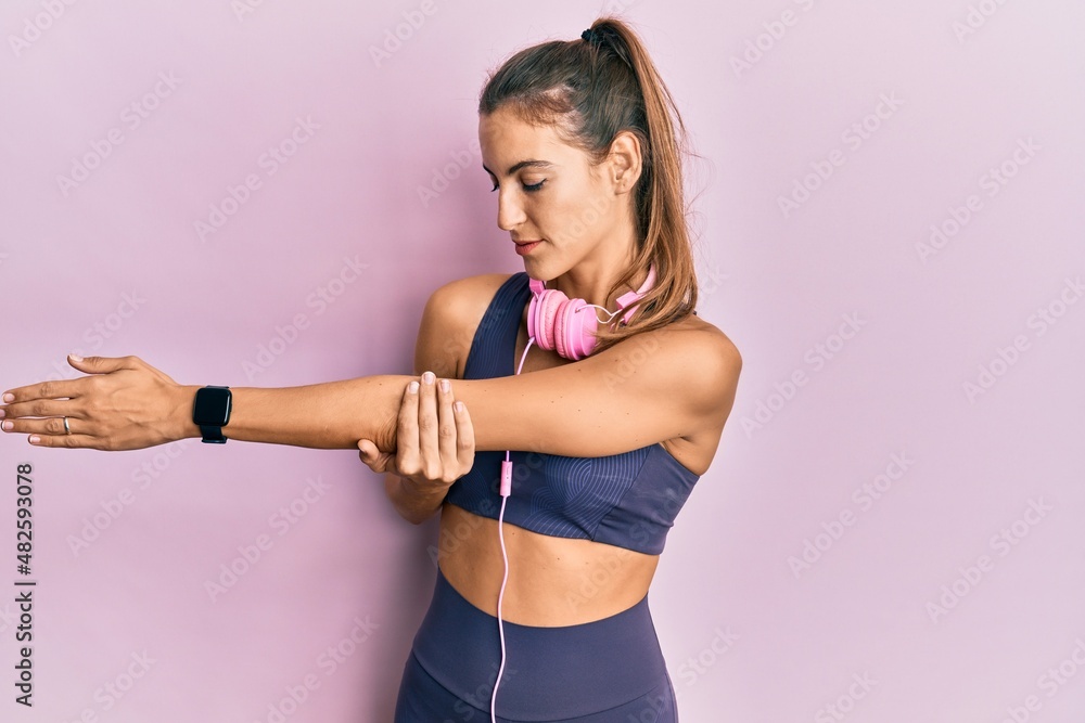 Young sportswoman stretching muscles after doing exercise wearing sporty clothes and headphones, standing doing flexibility activity Young sportswoman stretching muscles after doing exercise wearing sporty clothes and headphones, standing doing flexibility activity