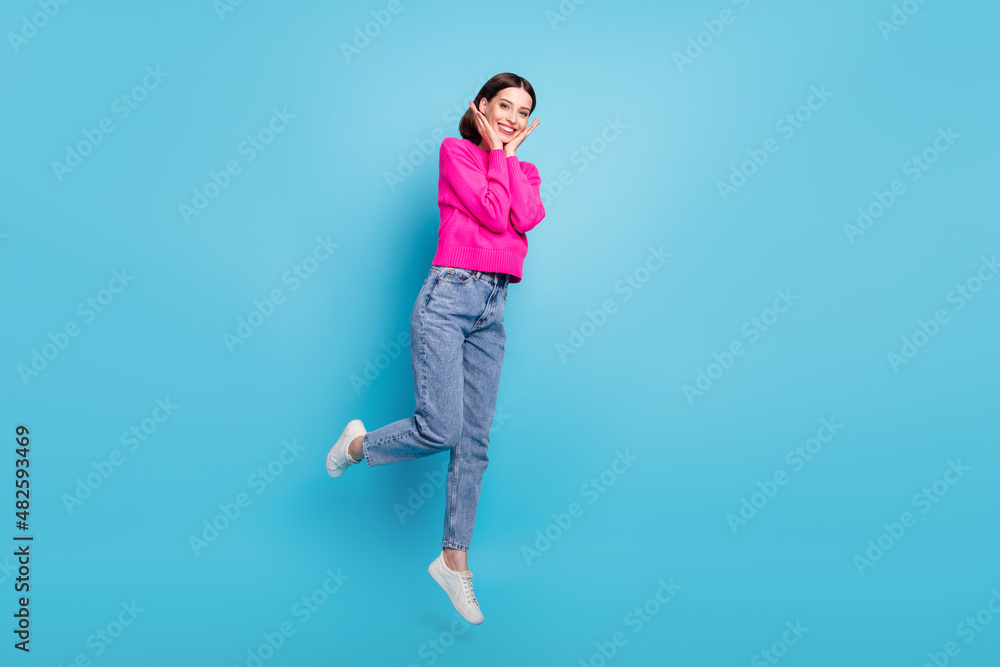 Photo of pretty impressed young lady wear pink pullover jumping high arms cheeks isolated blue color background Photo of pretty impressed young lady wear pink pullover jumping high arms cheeks isolated blue color background