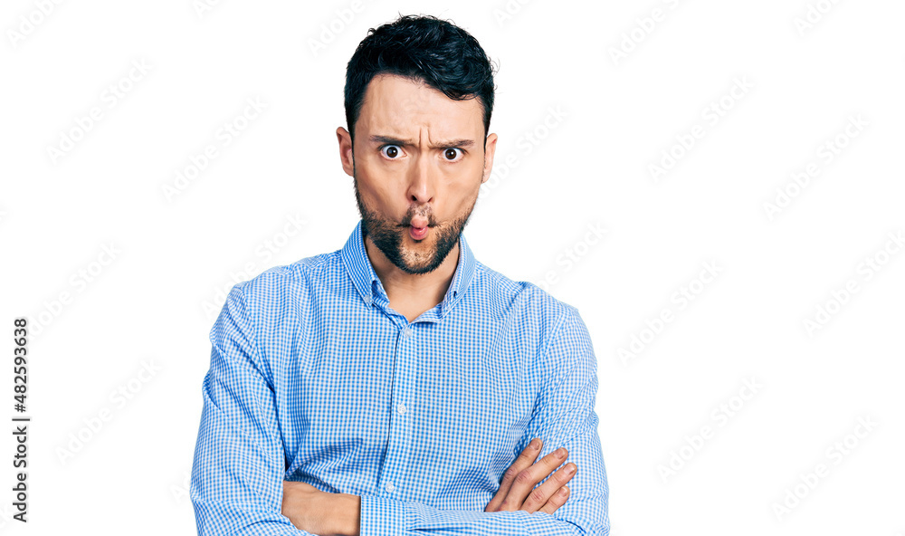 Hispanic man with beard with arms crossed gesture making fish face with mouth and squinting eyes, crazy and comical. Hispanic man with beard with arms crossed gesture making fish face with mouth and squinting eyes, crazy and comical.