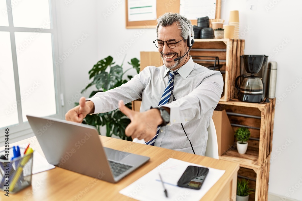 Middle age hispanic business man working at the office wearing operator headset approving doing positive gesture with hand, thumbs up smiling and happy for success. winner gesture. Middle age hispanic business man working at the office wearing operator headset approving doing positive gesture with hand, thumbs up smiling and happy for success. winner gesture.
