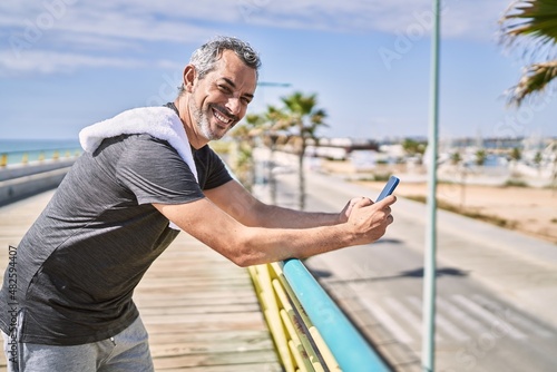 Middle age hispanic man wearing sportswear using smartphone at seaside