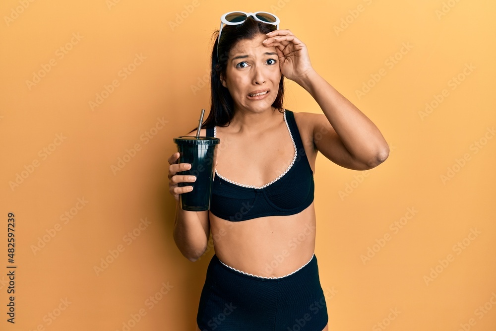 Young latin woman wearing bikini drinking soda stressed and frustrated with hand on head, surprised and angry face Young latin woman wearing bikini drinking soda stressed and frustrated with hand on head, surprised and angry face