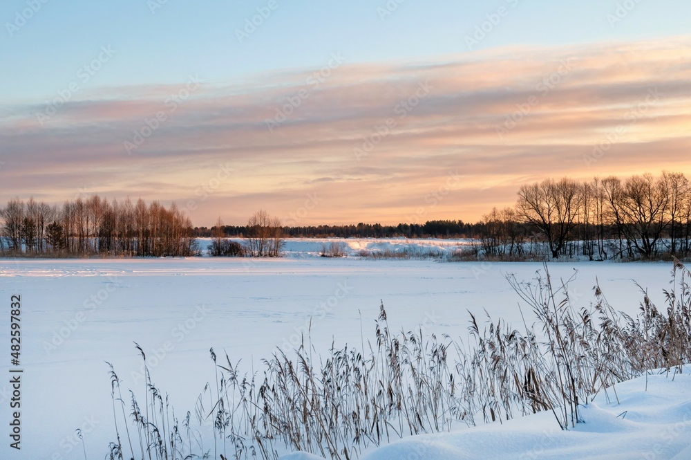 Beautiful winter landscape on frosty sunny morning. Frozen river under snow and trees in rays of morning rising sun. Pink sky Beautiful winter landscape on frosty sunny morning. Frozen river under snow and trees in rays of morning rising sun. Pink sky