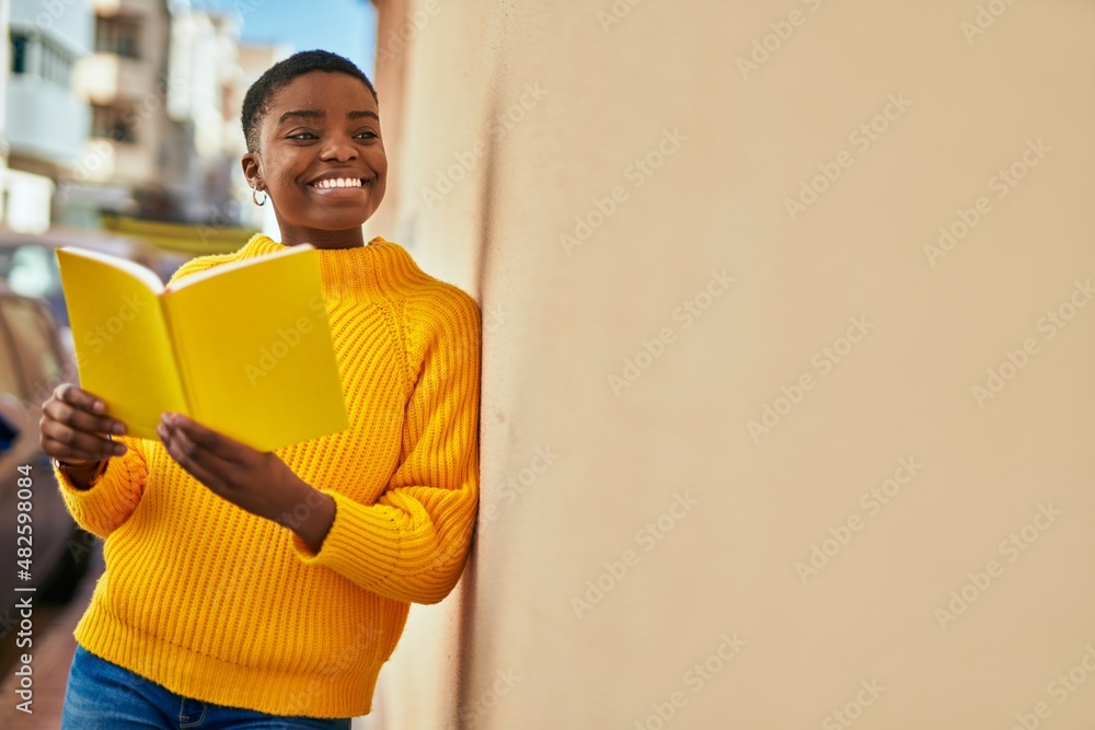 Young african american woman smiling happy reading book at the city.