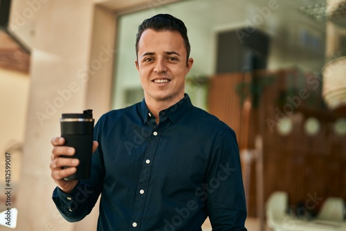 Young hispanic man smiling happy drinking coffee at the city.