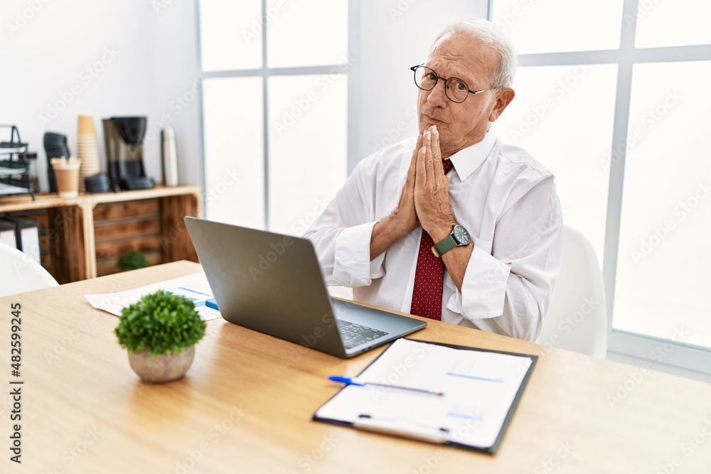 Senior man working at the office using computer laptop praying with hands together asking for forgiveness smiling confident. Senior man working at the office using computer laptop praying with hands together asking for forgiveness smiling confident.