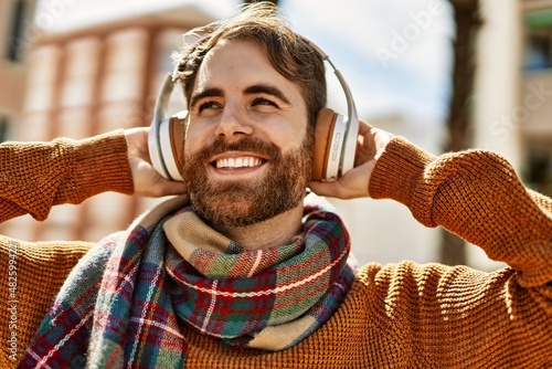 Fotobehang Young caucasian man with beard listening to music wearing headphones outdoors on